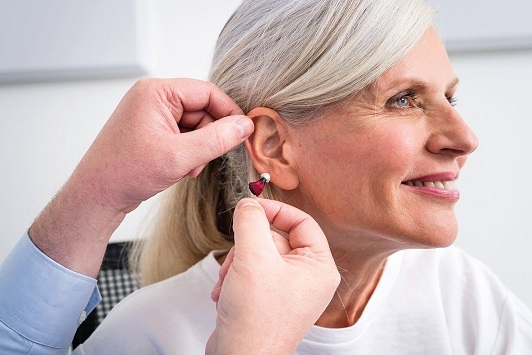 Ältere Frau erhält ein modernes Hörgerät, Hörakustiker passt Hörhilfe am Ohr an.